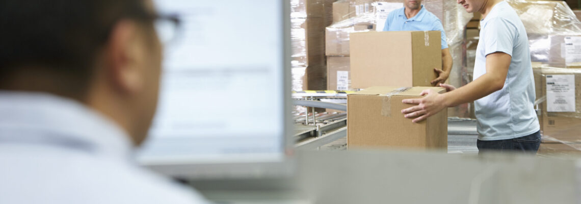 Warehouse workers package orders in boxes while a man uses an ERP on the computer.