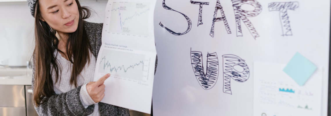 a woman gives a presentation while a poster next to her reads "Start Up"