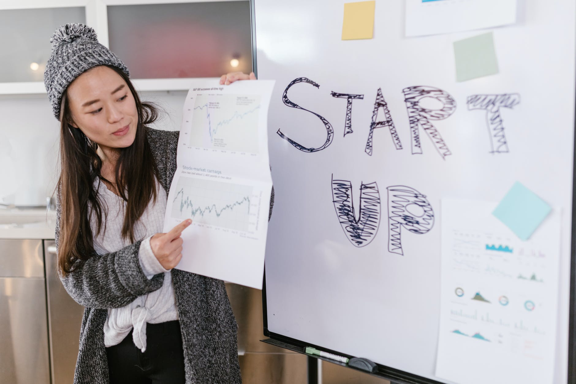 a woman points to a graph of data while a poster next to her reads "Start Up"